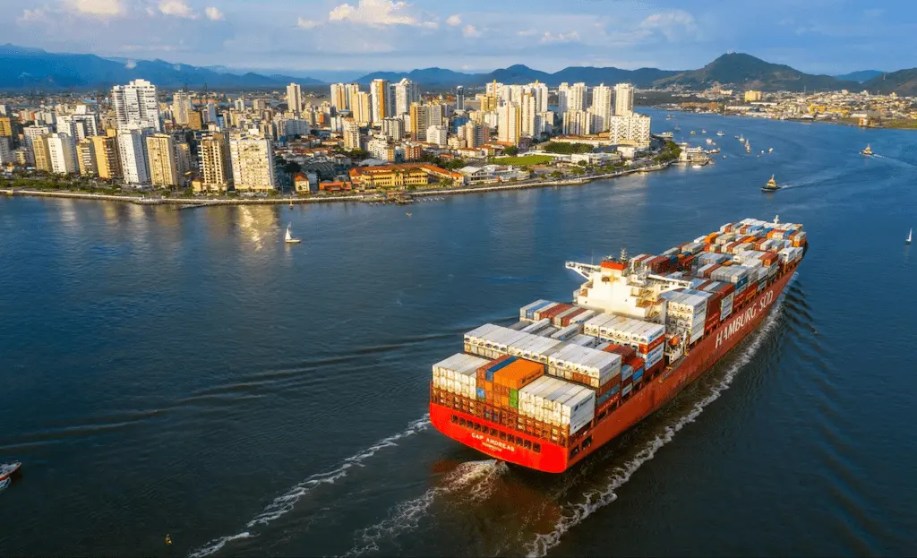 Navio cargueiro repleto de contêineres navegando rumo ao porto, representando o fluxo internacional ligado às siglas de logística de importações