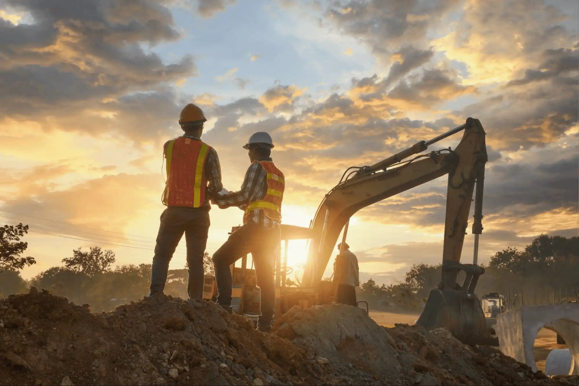 Engenheiros e operários da construção civil em canteiro de obras, com escavadeira ao fundo.